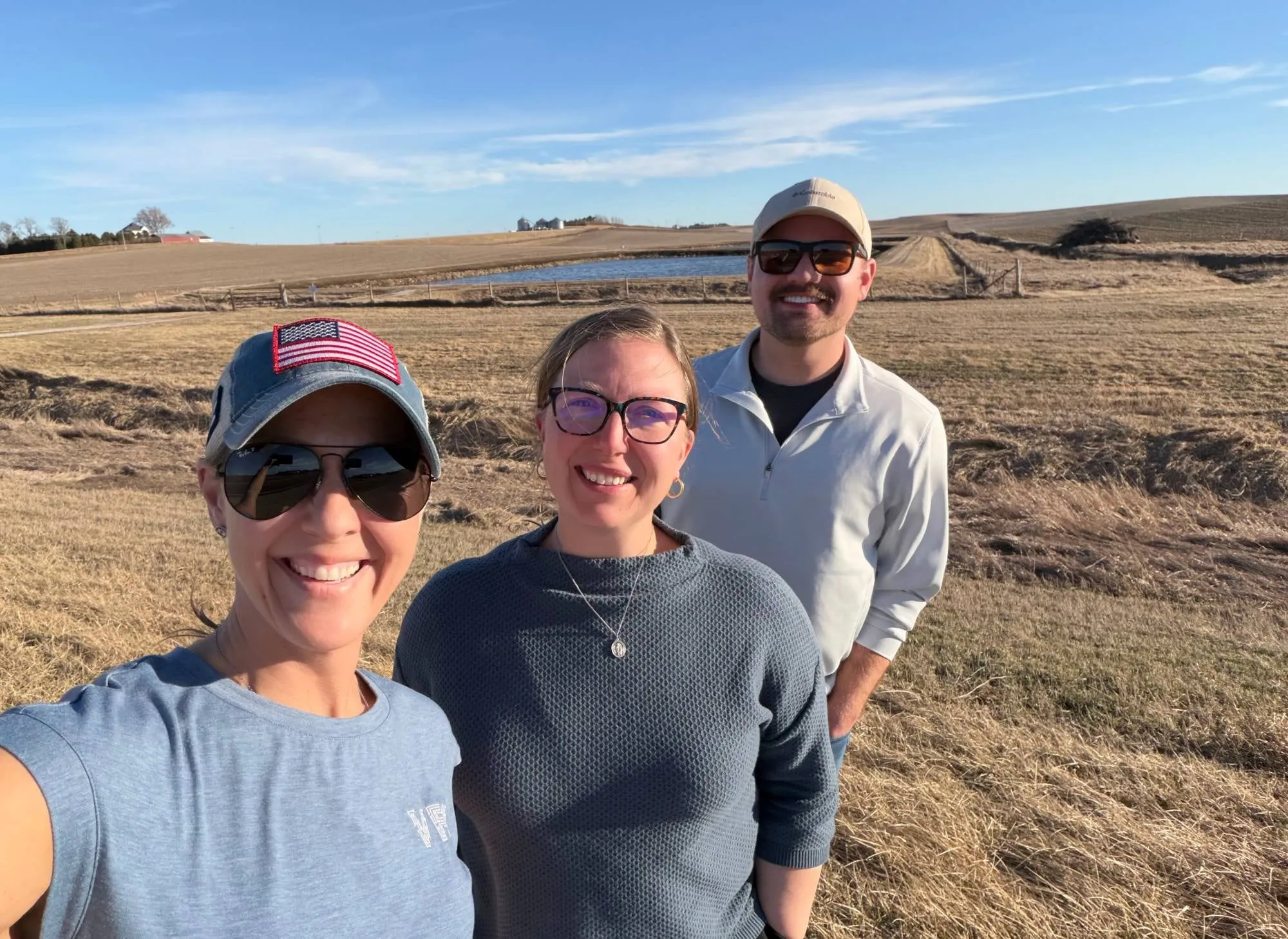 Three VFO team members smiling outdoors in open farmland on a sunny day.