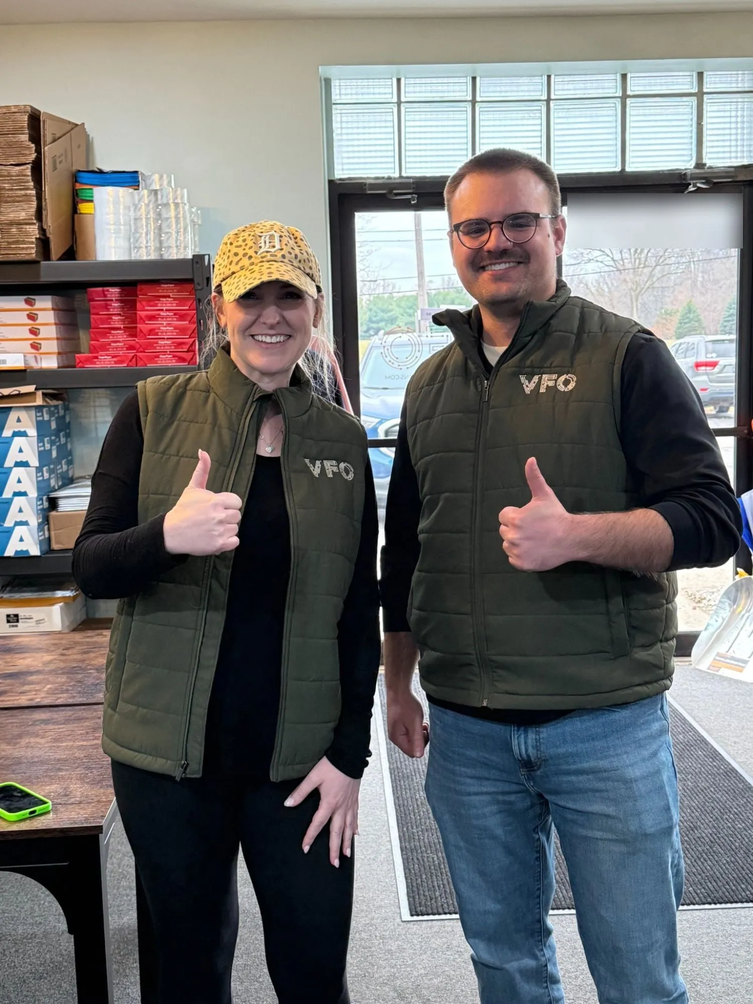 Two VFO team members in VFO vests giving a thumbs-up at the VFO office.