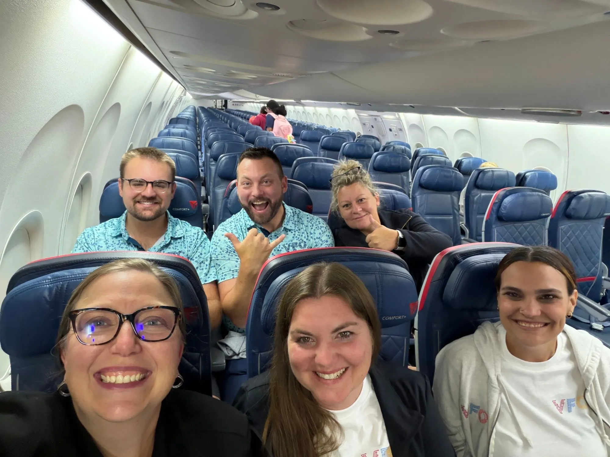 Six VFO team members smiling on a flight, traveling together.